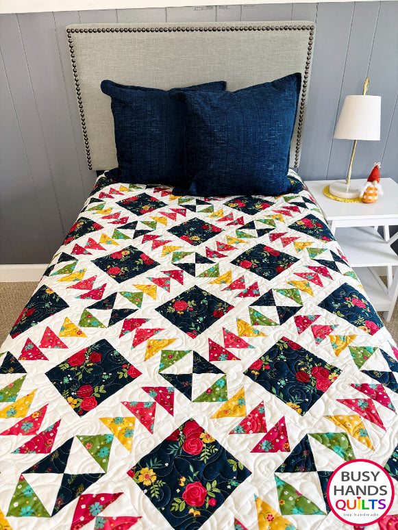 A colorful patchwork quilted blanket with floral and geometric blocks in navy, red, orange, yellow, and green autumn colors. Gift ideas men and women for birthdays, Christmas, Housewarming, and Wedding Gifts for Brides and Grooms.