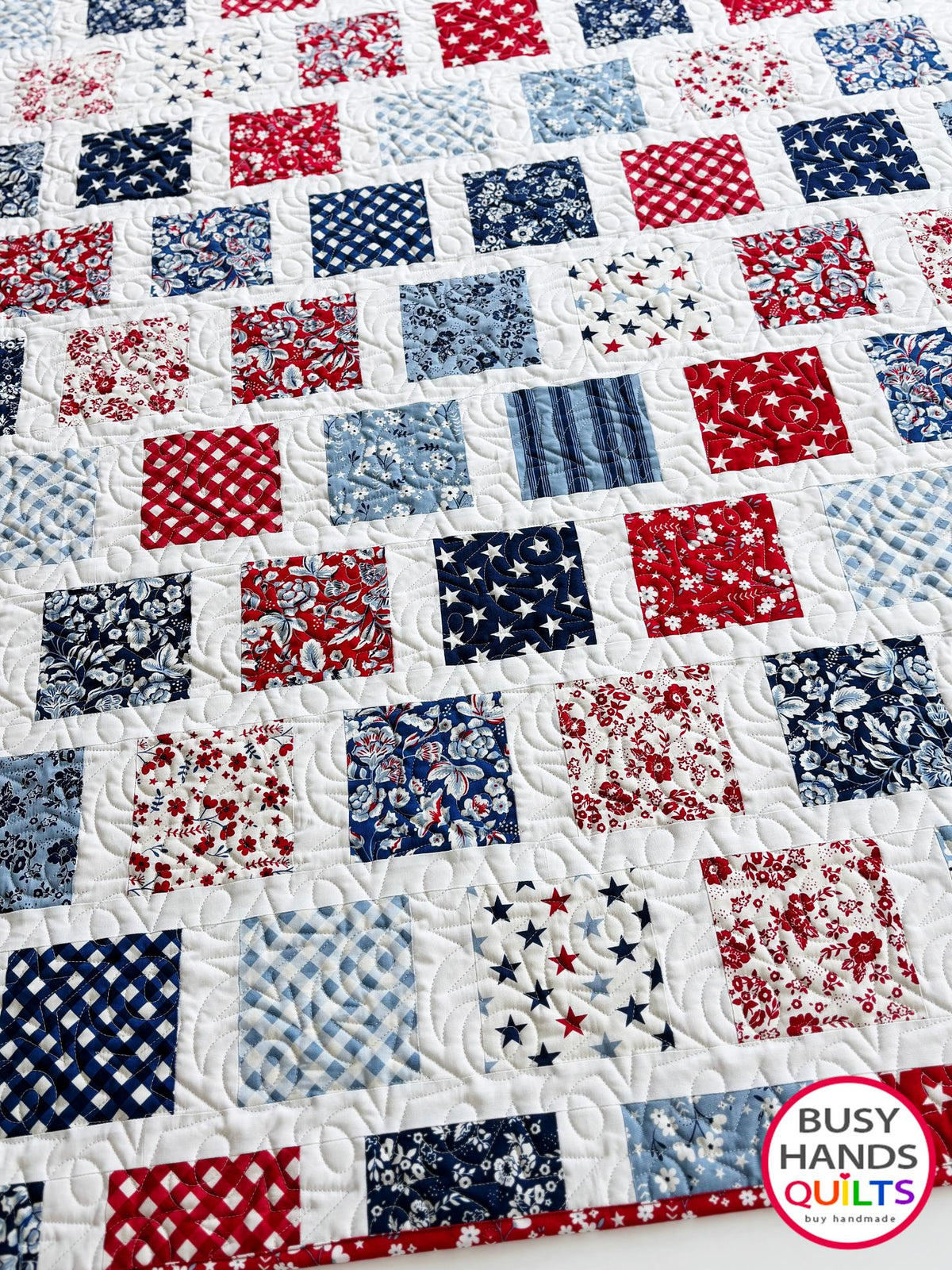A patriotic-themed patchwork quilted bedspread with red, white, and blue squares. Americana throw sofa blanket, decor for 4th of July stars and summer. Gift ideas for birthdays, Christmas, housewarming, and wedding gifs for brides and grooms.