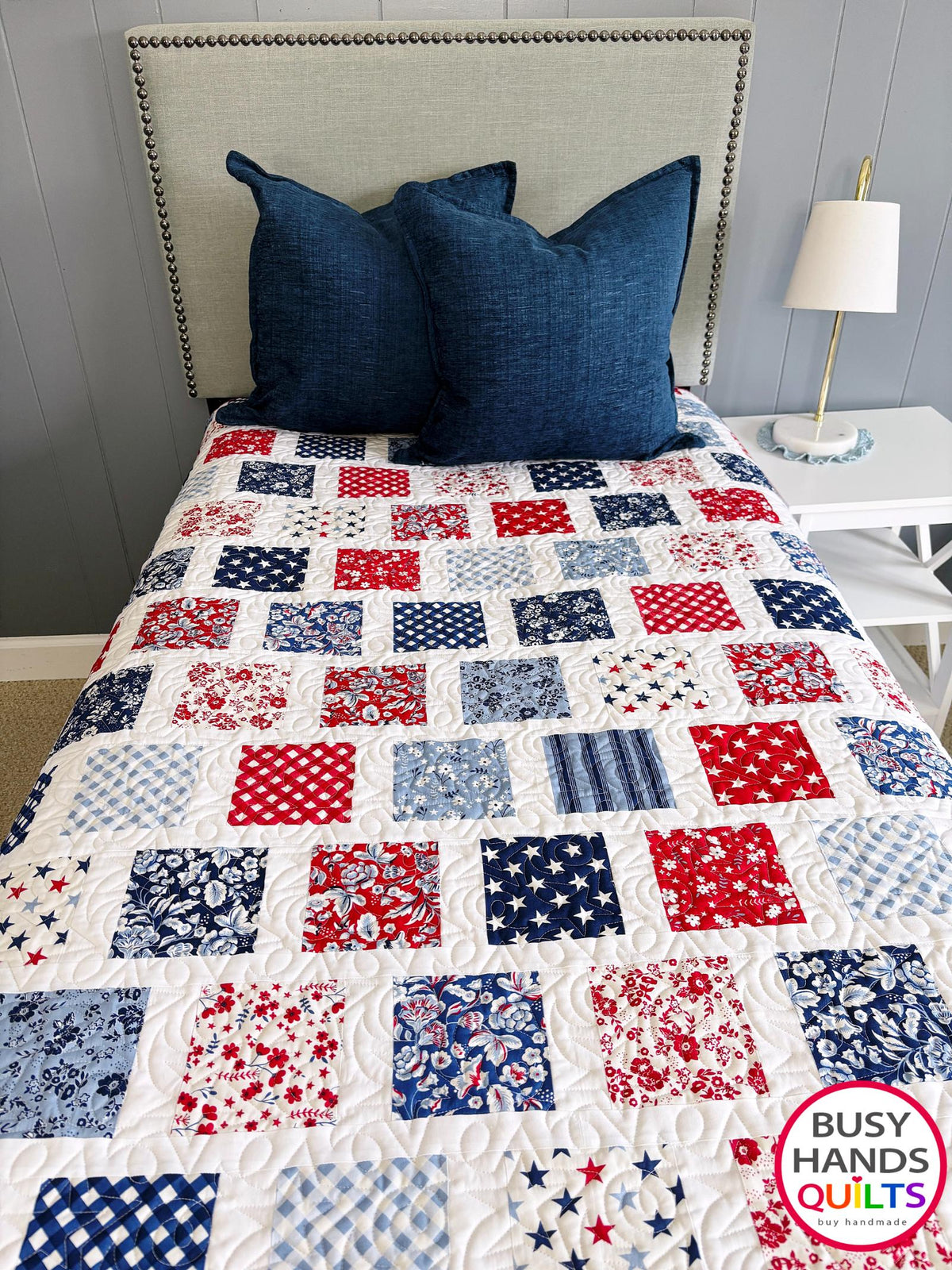 A patriotic-themed patchwork quilted bedspread with red, white, and blue squares. Americana throw sofa blanket, decor for 4th of July stars and summer. Gift ideas for birthdays, Christmas, housewarming, and wedding gifs for brides and grooms.
