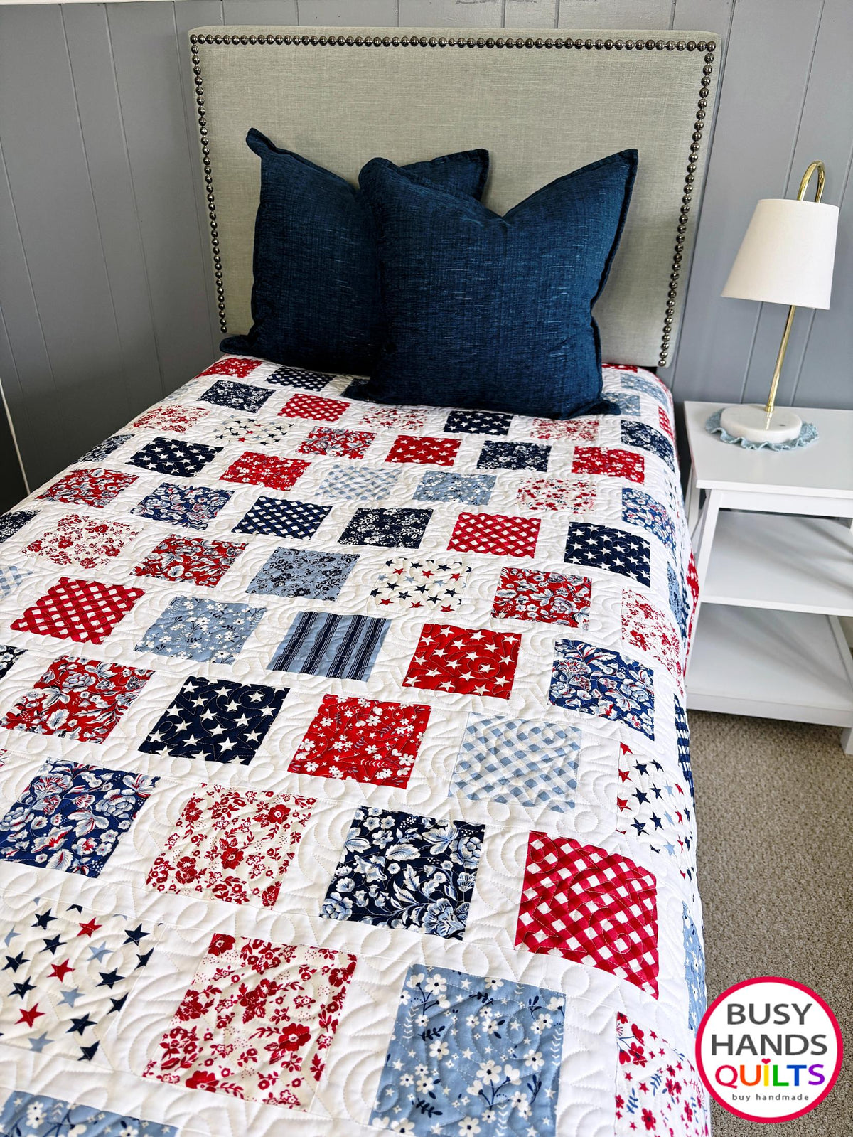A patriotic-themed patchwork quilted bedspread with red, white, and blue squares. Americana throw sofa blanket, decor for 4th of July stars and summer. Gift ideas for birthdays, Christmas, housewarming, and wedding gifs for brides and grooms.