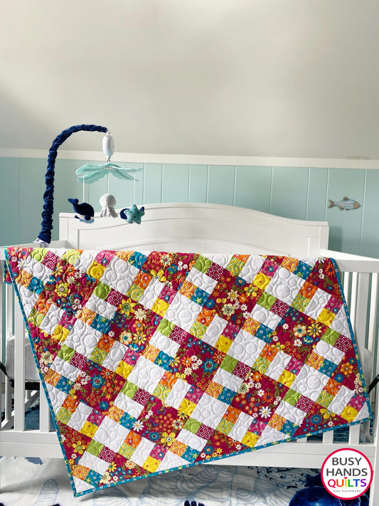 Handmade, heirloom-quality baby girl quilt in fuchsia pink floral with teal, yellow, orange, and green accents, hanging over a crib in a nursery. Perfect for a baby shower gift idea or Christmas present idea 